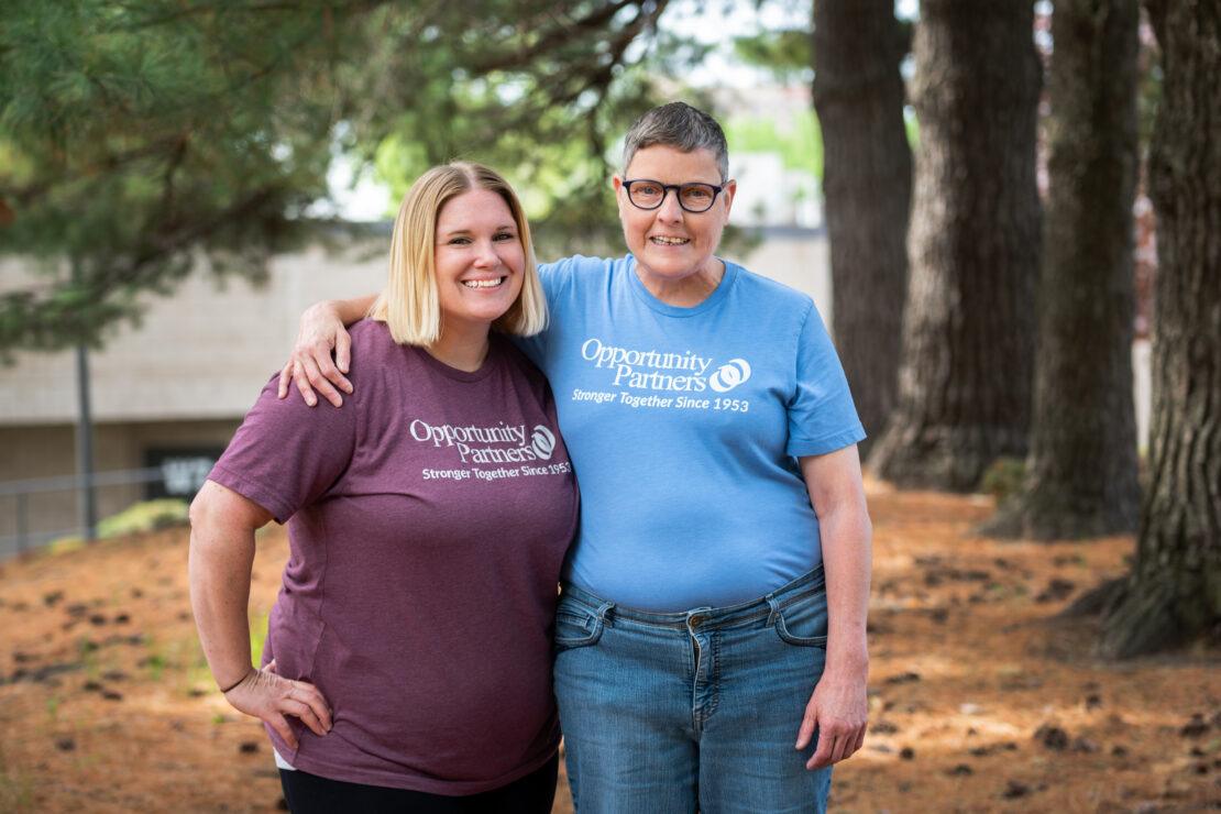 Staff and person served smiling with arms around each other outside