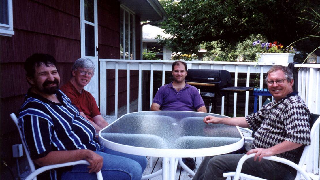 Four men sitting around table outside on a deck