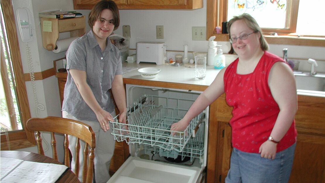 Two women in a kitchen smiling next to the dishwasher
