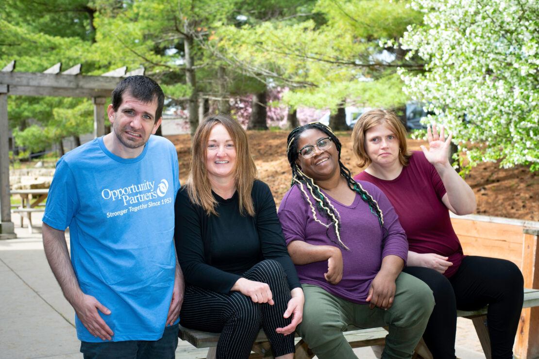 Group of people outside smiling and sitting on a picnic table