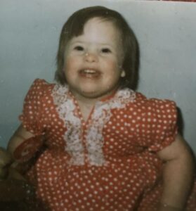An old photo of a young girl with Down syndrome smiling