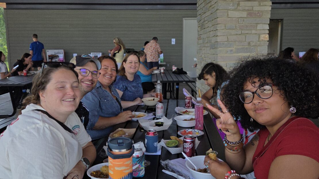 A group of people witting at a picnic table and smiling at the camera